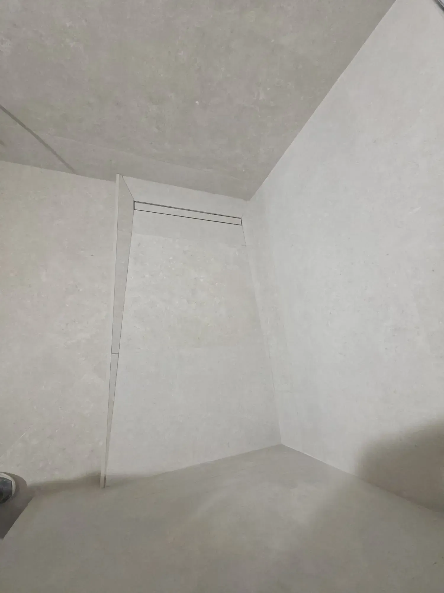 Rincón blanco y desnudo de una habitación con techo inclinado y una pequeña rejilla de ventilación
