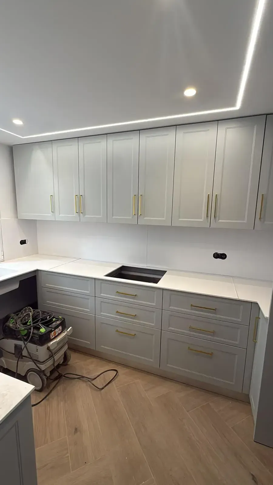 Cocina moderna blanca con armarios inferiores grises, placa de cocción integrada e iluminación de tiras en el techo.