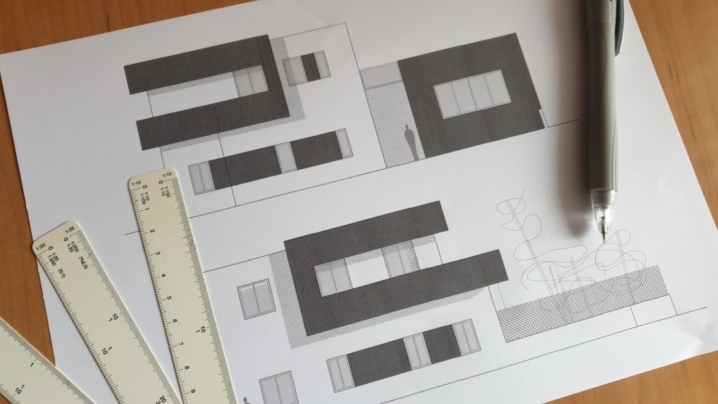 Herramientas de dibujo y regla sobre un escritorio junto a una hoja con bocetos de diseños geométricos grises.