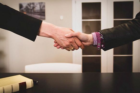 Dos personas se dan la mano sobre una mesa.