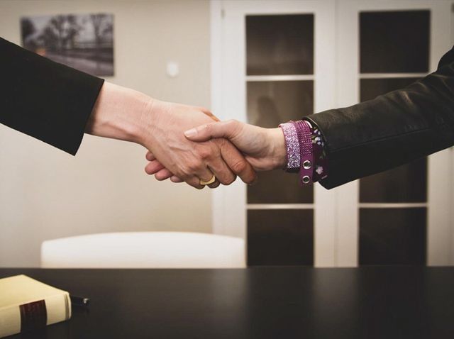 Dos personas se dan la mano sobre una mesa.