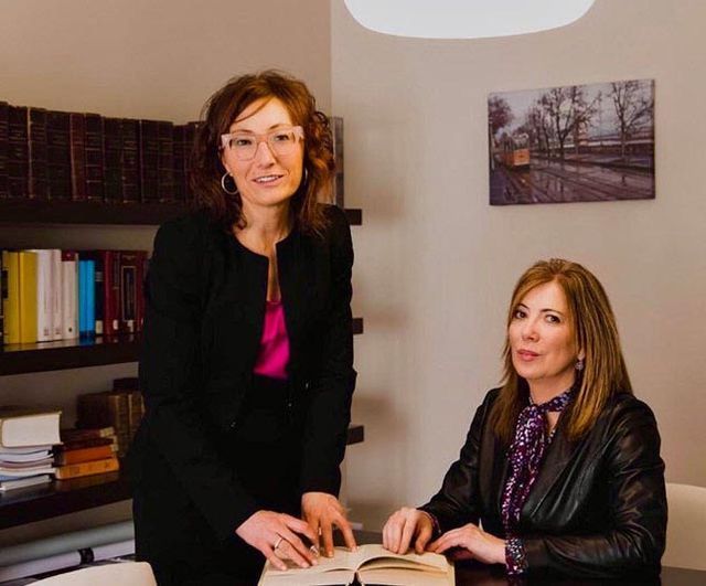 Dos mujeres están paradas una al lado de la otra y una está leyendo un libro.