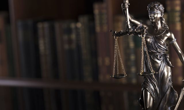 Una estatua de la justicia está parada frente a una estantería que sostiene una balanza de la justicia.