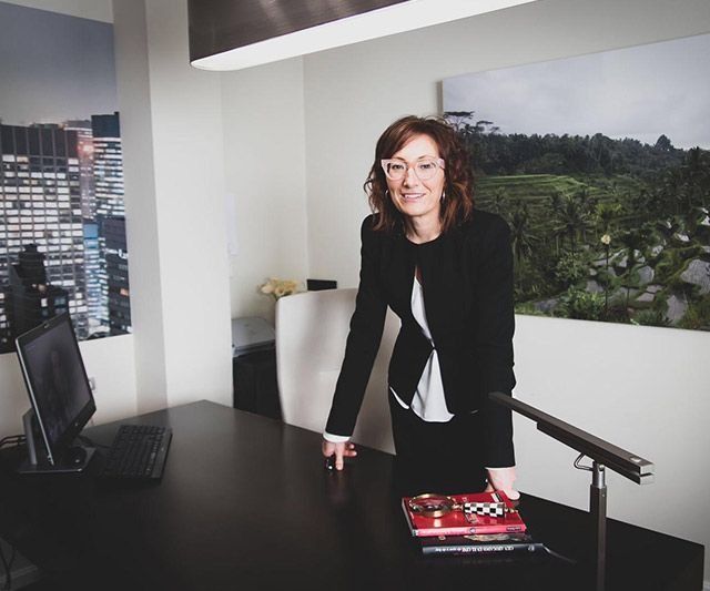 Una mujer con un traje negro está parada frente a un escritorio.