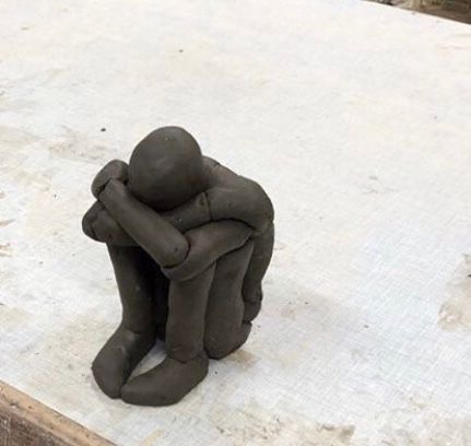Una escultura de arcilla de un hombre sentado con la cabeza entre las manos.