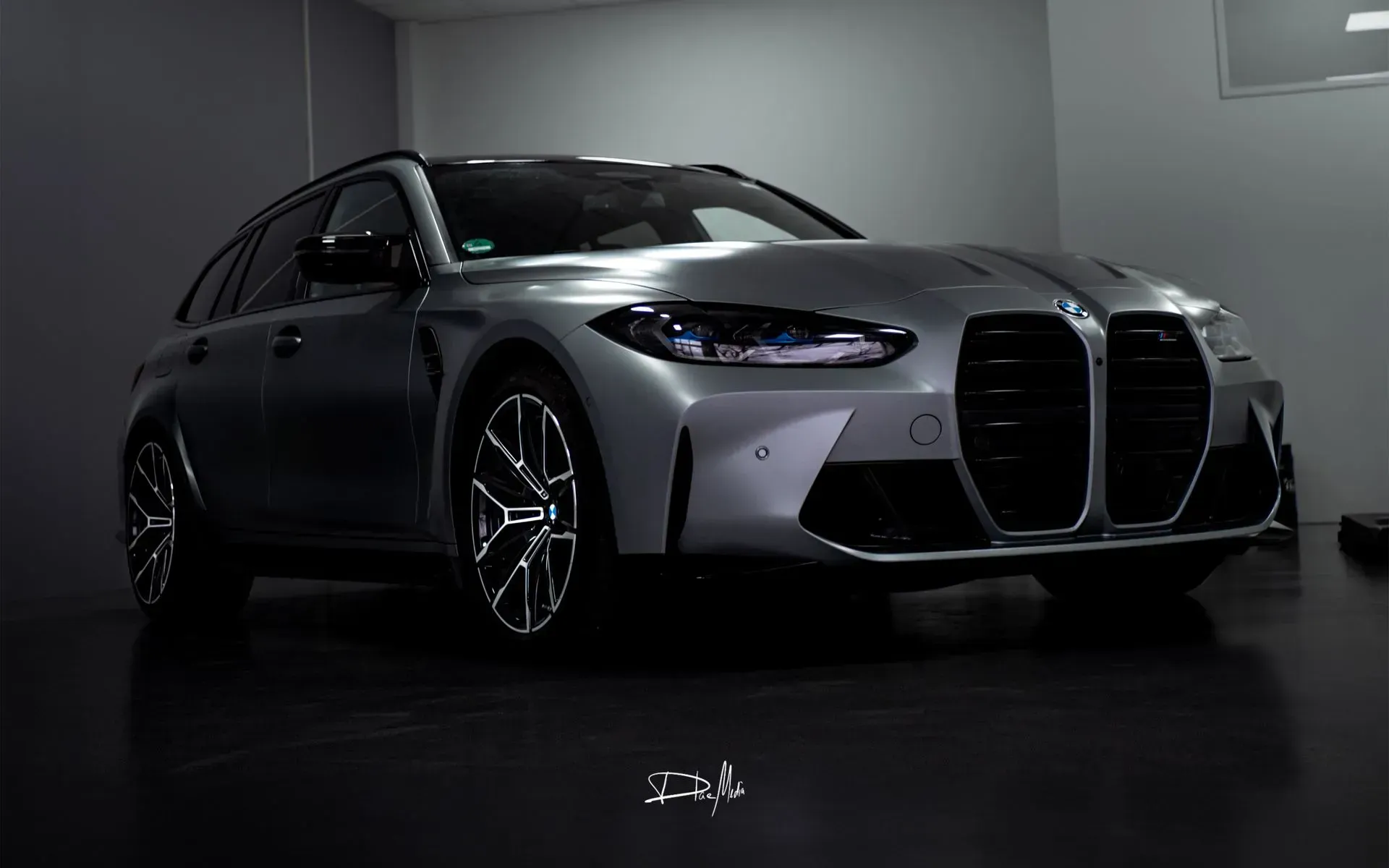 Ein silberner BMW M3 steht in einem dunklen Raum.