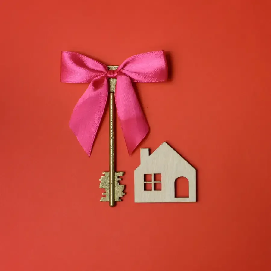 Una llave con un lazo rosa y una casa de madera sobre un fondo rojo.