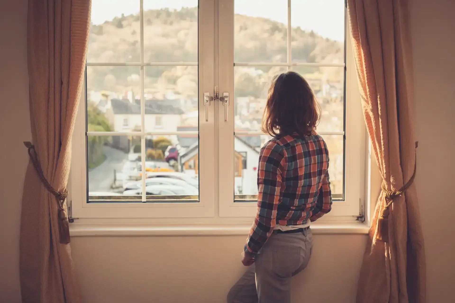 Una mujer está parada frente a una ventana mirando hacia afuera.