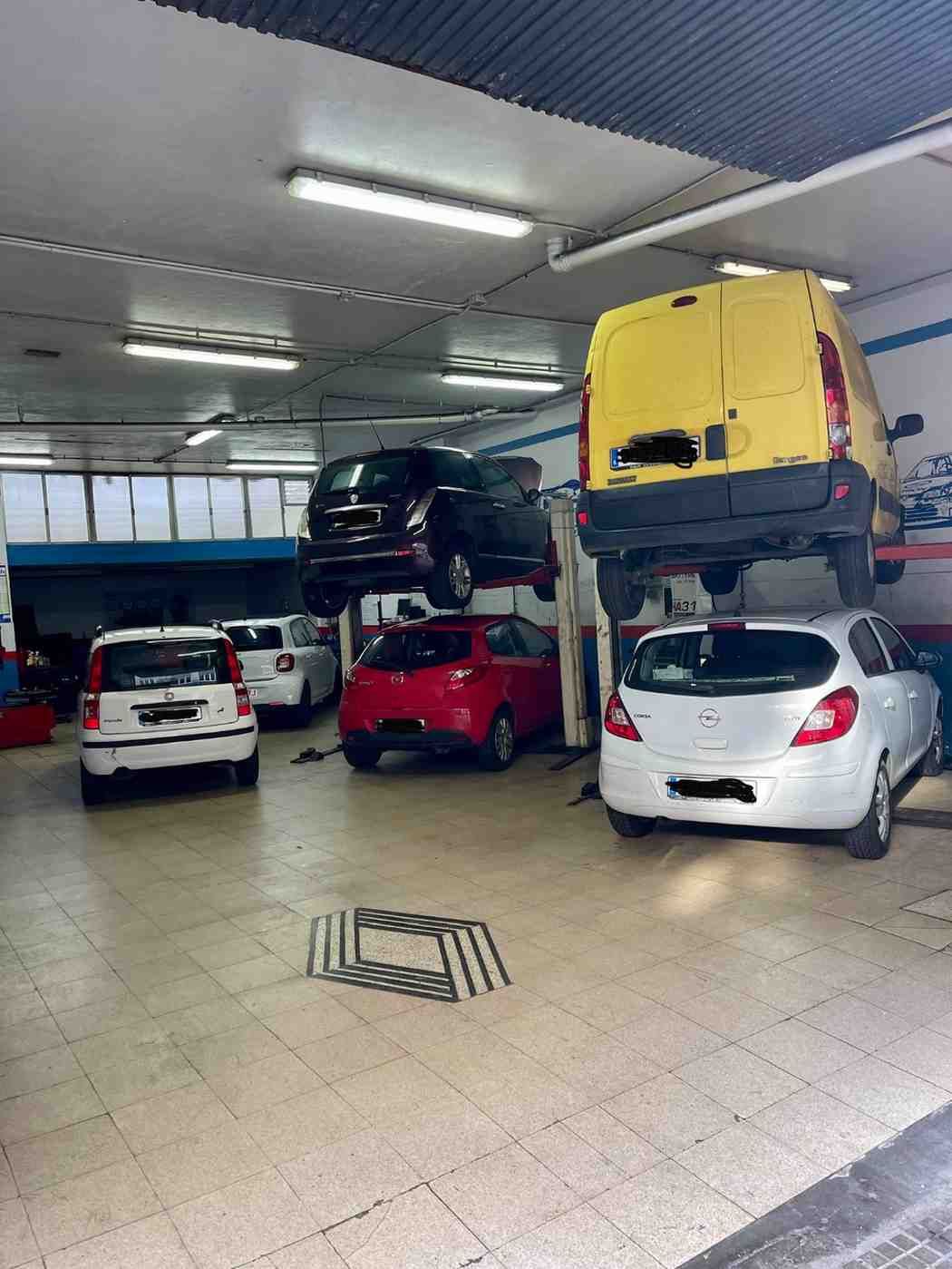 Un taller mecánico bien iluminado con varios coches sobre elevadores y aparcados en el suelo de hormigón.