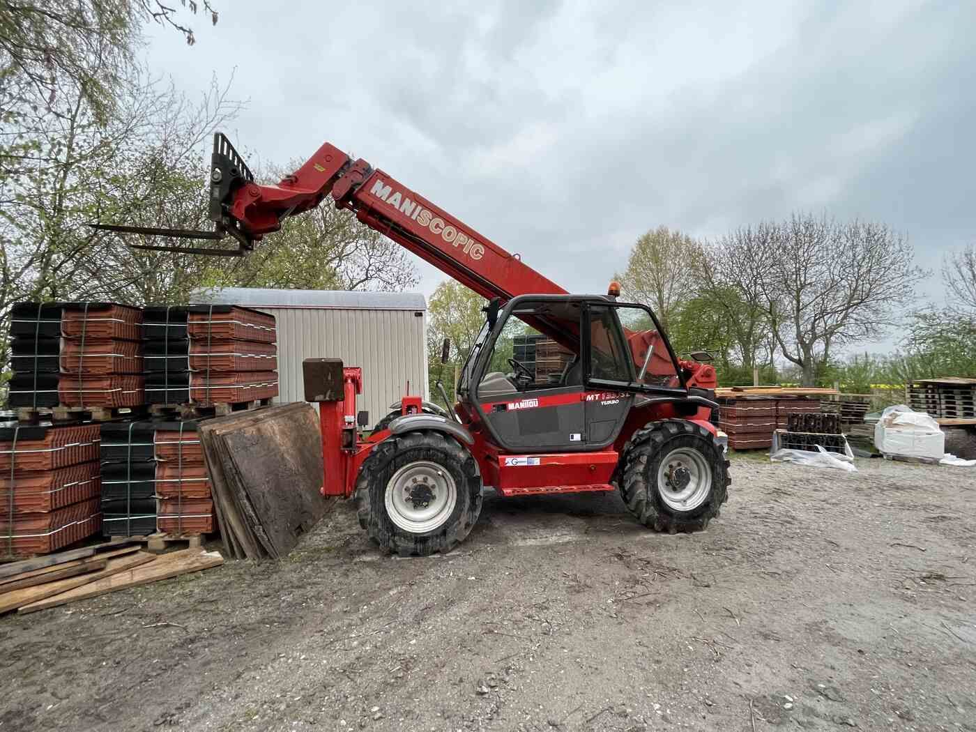 Ein roter Gabelstapler steht auf einem unbefestigten Parkplatz neben einem Ziegelhaufen.