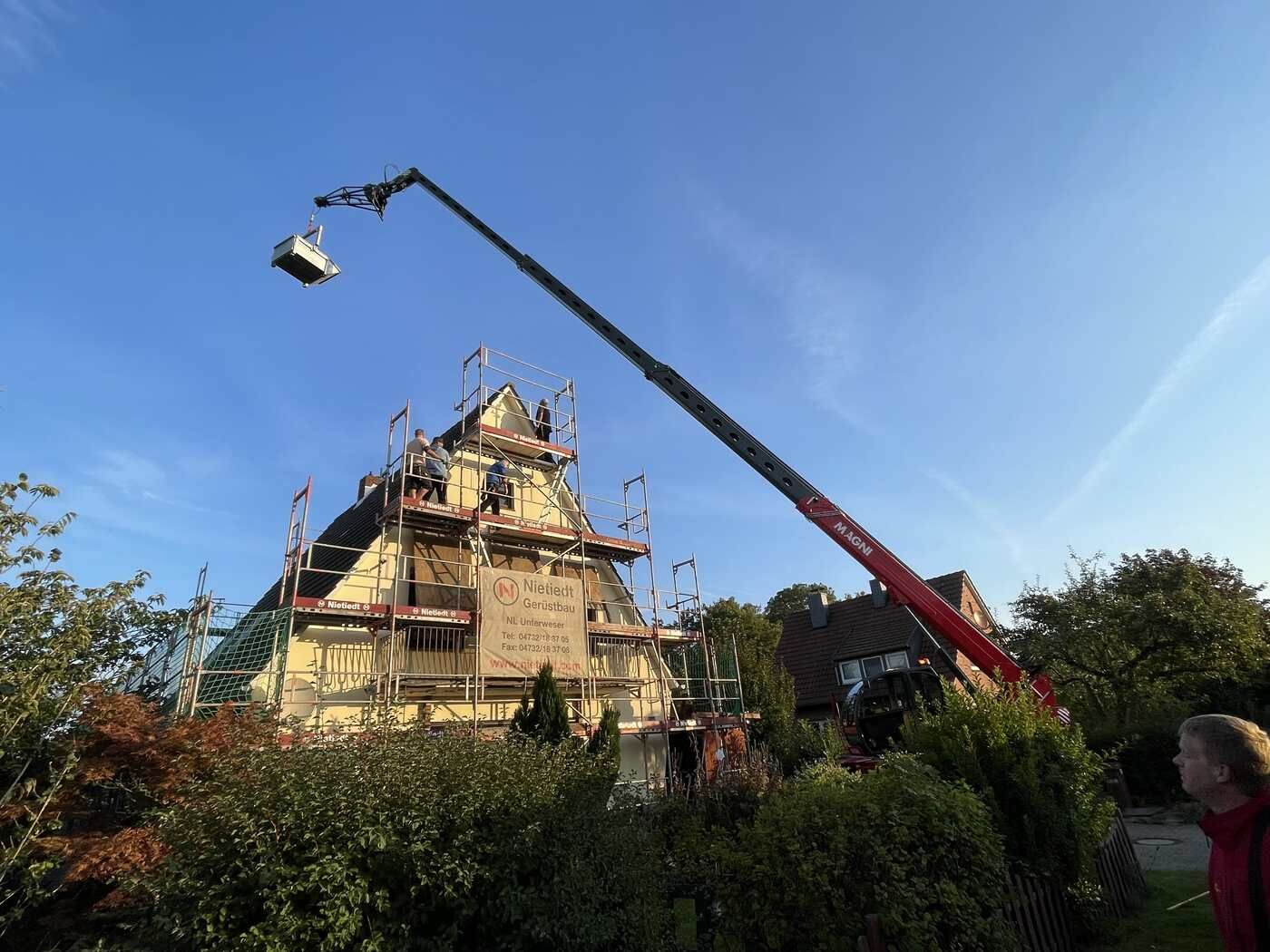 Mit einem Kran wird ein großes Objekt über ein im Bau befindliches Gebäude gehoben.