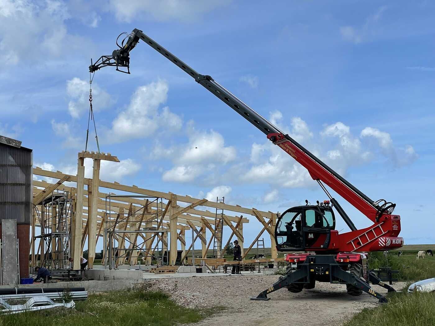 Ein Kran hebt ein Stück Holz vor einem im Bau befindlichen Gebäude an.