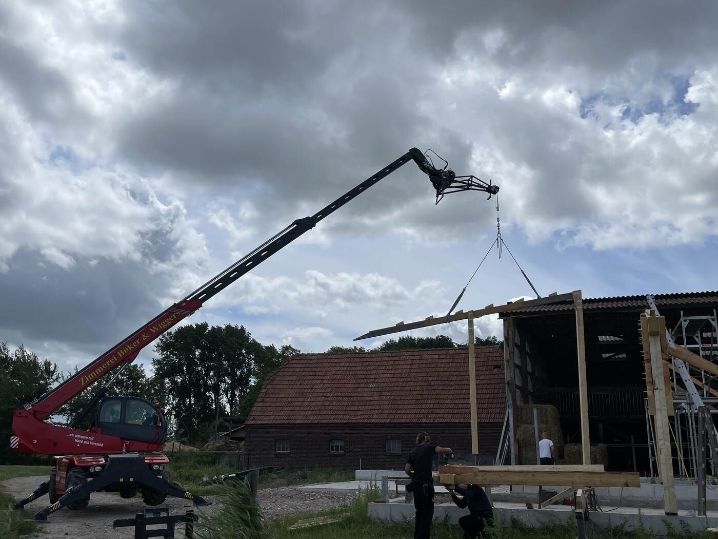 Ein Kran hebt ein Stück Holz vor einem Gebäude an.