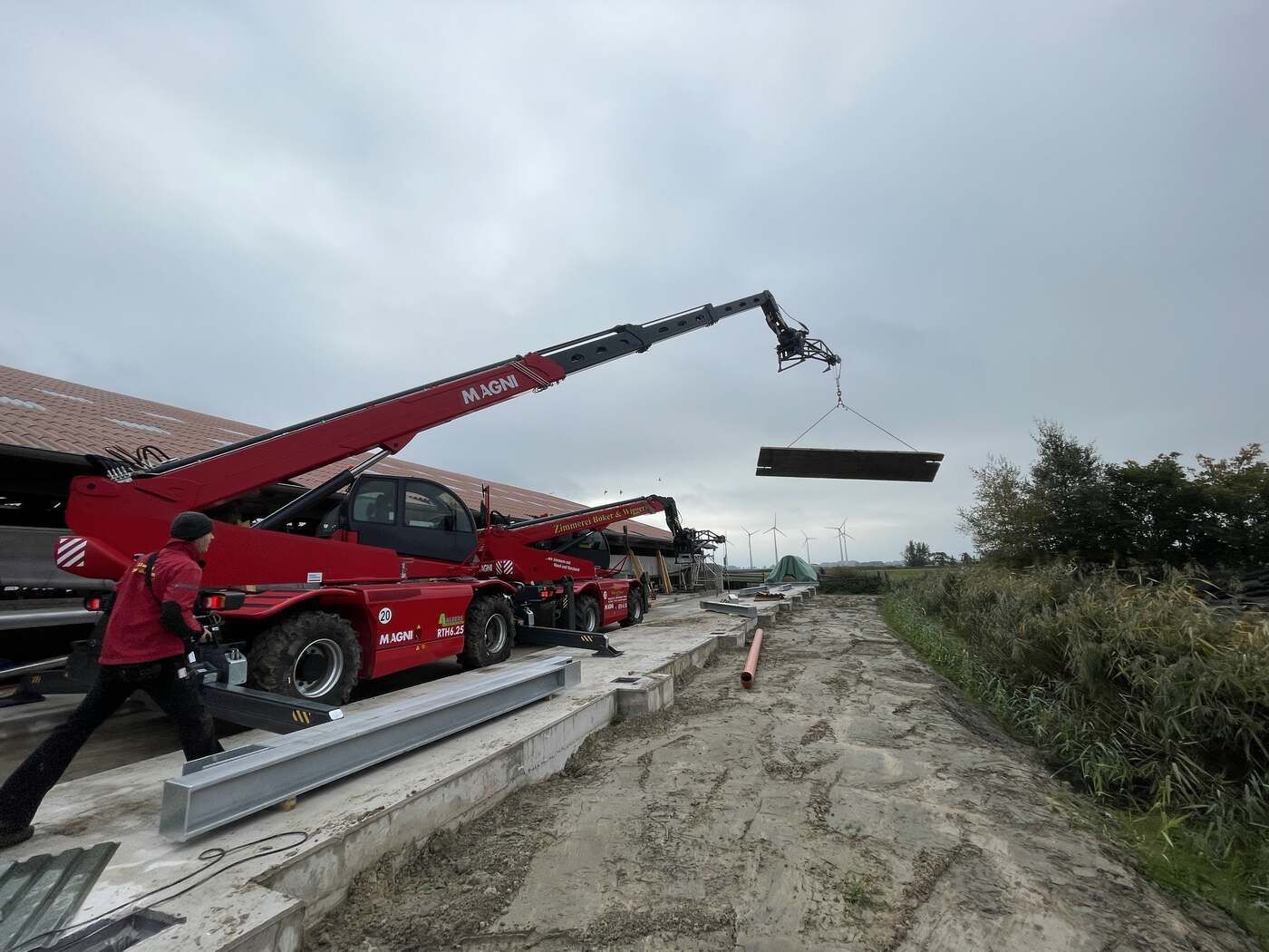 Ein Kran hebt ein großes Stück Metall auf einen Feldweg.