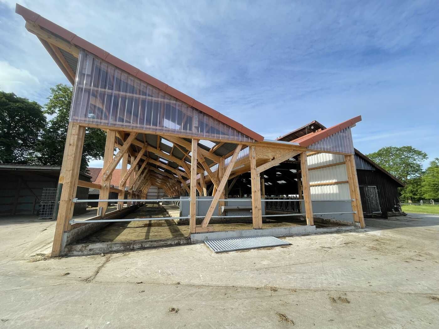 Auf einem Bauernhof wird eine große Holzkonstruktion mit einem roten Dach errichtet.