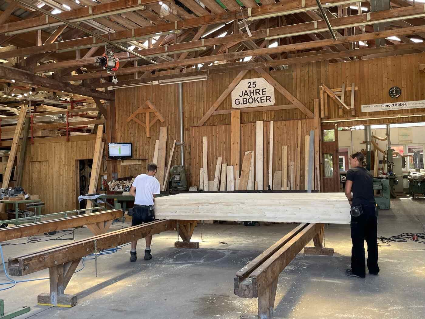 In einer Holzwerkstatt steht ein Mann neben einem großen Stück Holz.