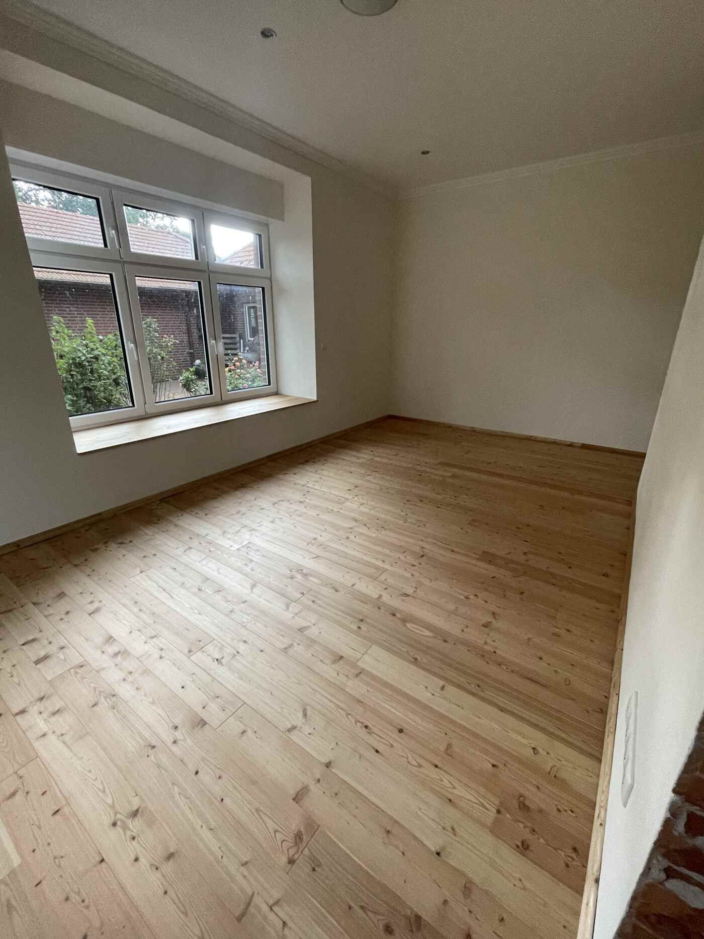 Ein leerer Raum mit Holzboden und einem großen Fenster.