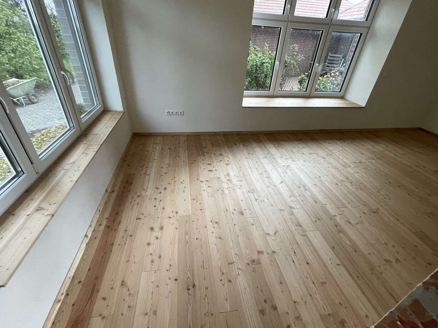 Ein leerer Raum mit Holzboden und zwei Fenstern.