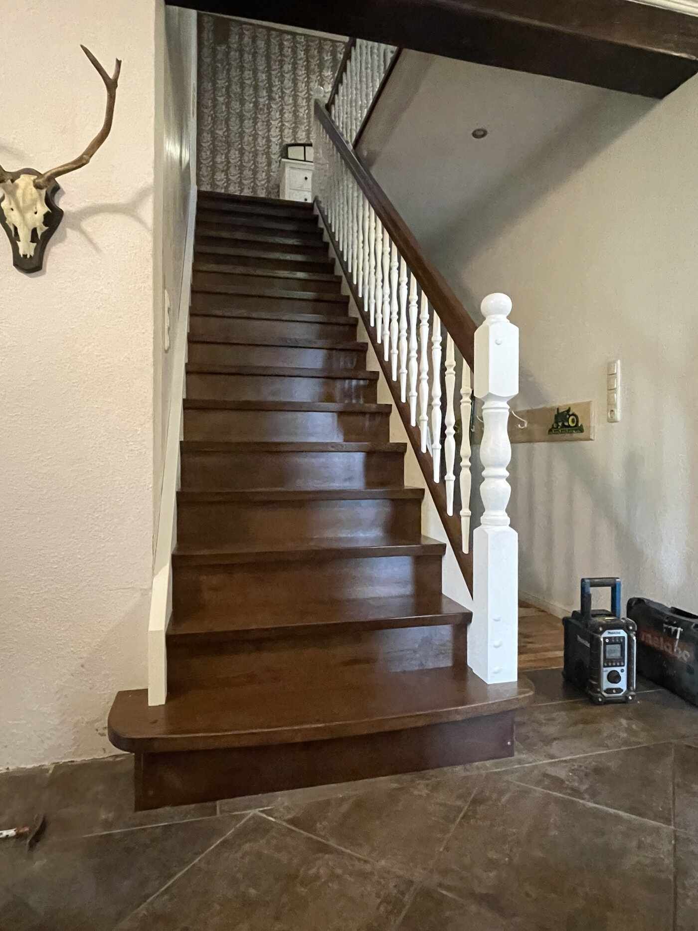 Eine Holztreppe mit weißem Geländer und einem Hirschkopf an der Wand.