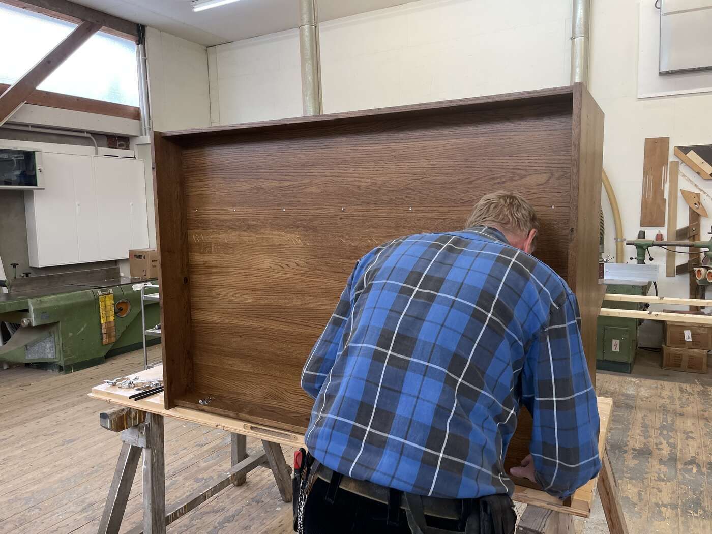 Ein Mann in einem blau karierten Hemd arbeitet an einem Stück Holz.