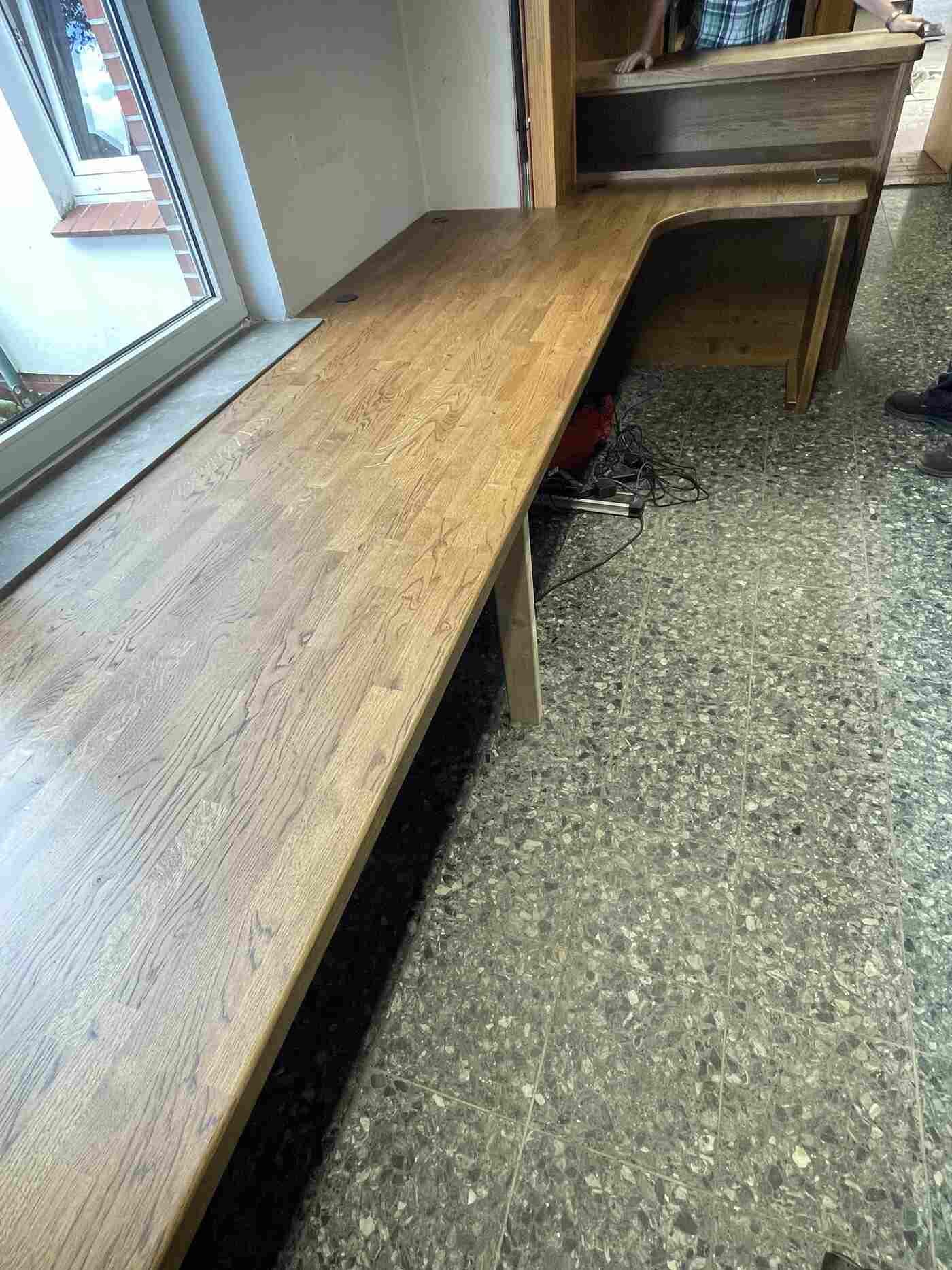 Eine Holzbank steht neben einem Fenster in einem Zimmer.