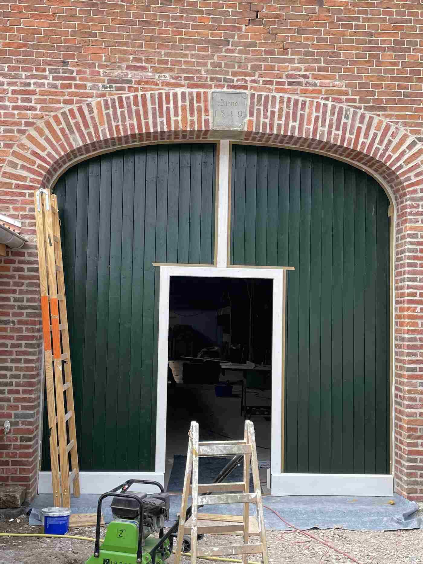 An einem Backsteingebäude wird eine grüne Tür angebracht.