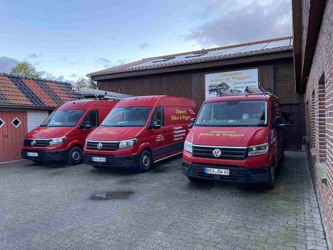 Drei rote Lieferwagen parken vor einem Backsteingebäude.