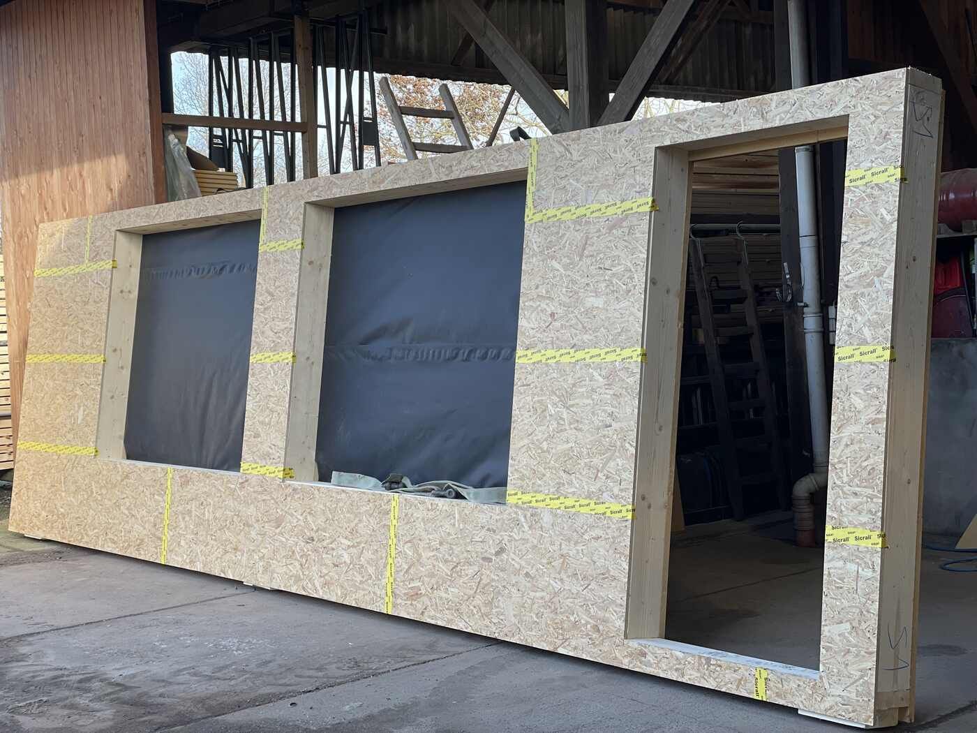 Vor einem Gebäude liegt ein großes Stück Holz auf dem Boden.