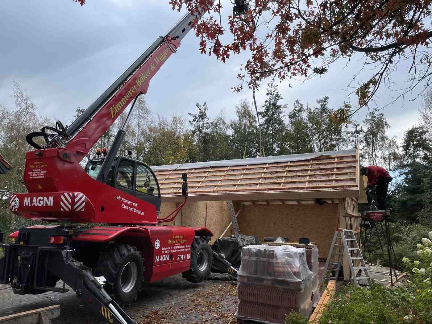 Mit einem roten Kran wird ein Dach auf einem Gebäude montiert.