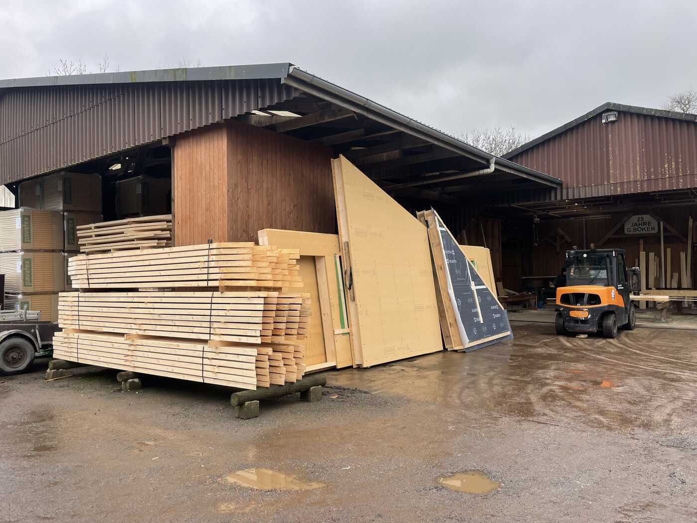 Vor einem Gebäude liegt ein großer Stapel Holz.