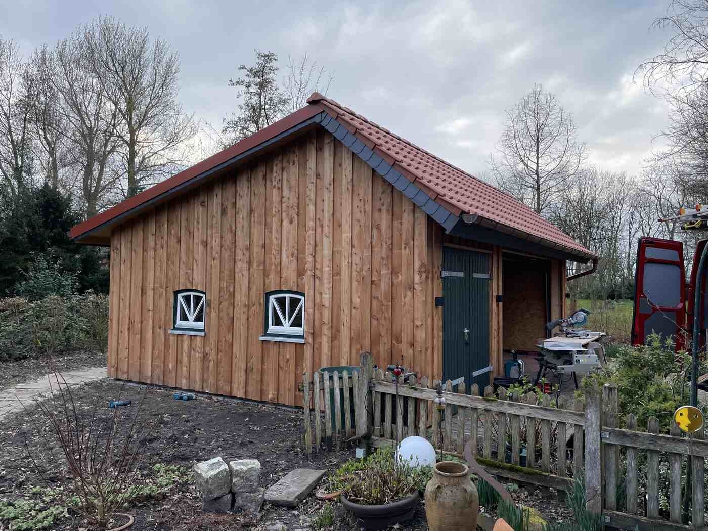 Ein kleines Holzhaus mit einem roten Dach steht mitten auf einem Feld.