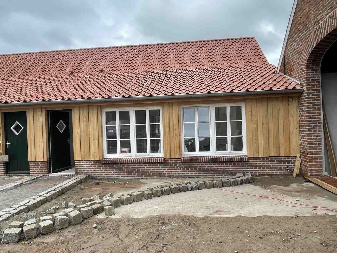 Es wird ein Haus mit rotem Ziegeldach und Holzverkleidung gebaut.