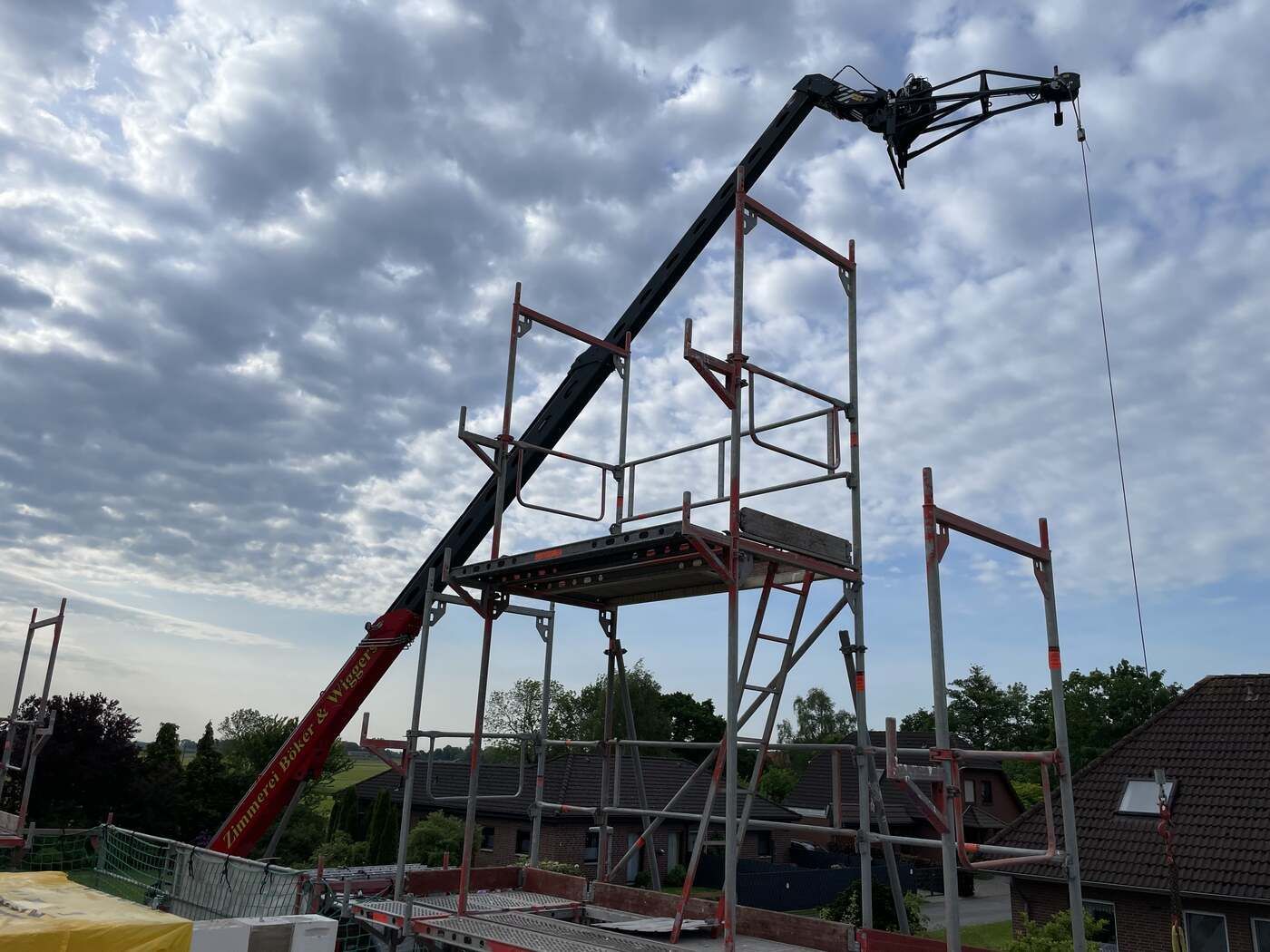 Ein Kran hebt ein Gerüst auf ein im Bau befindliches Gebäude.