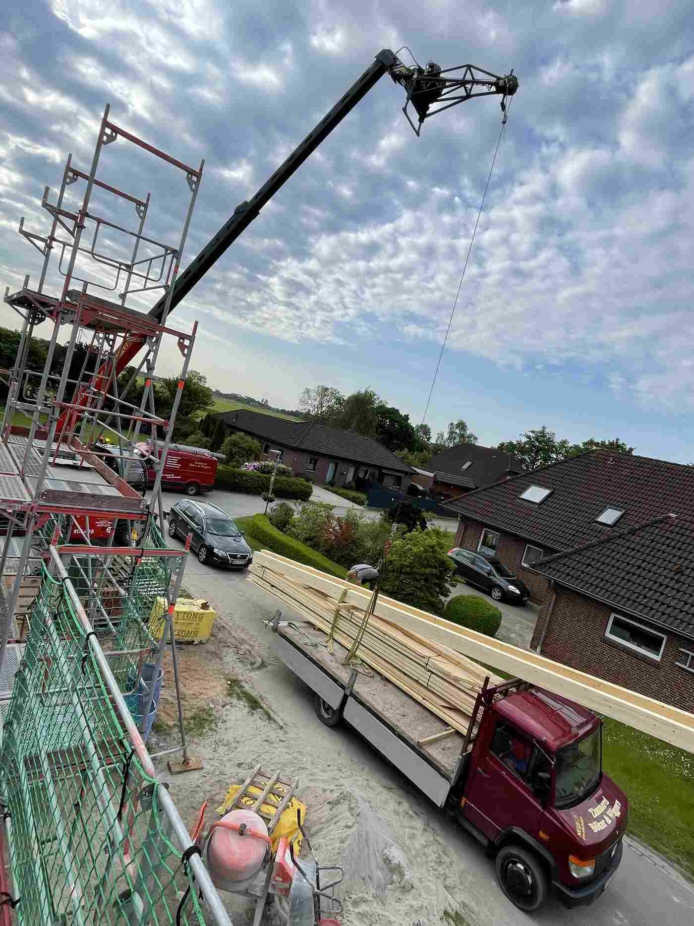 Ein roter Lastwagen transportiert Holzbretter auf einer Baustelle.