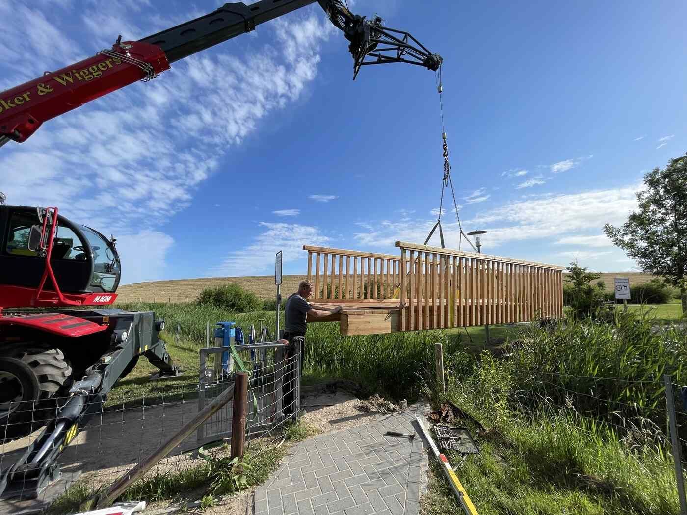 Ein Kran hebt eine Holzkonstruktion auf einem Feld an.