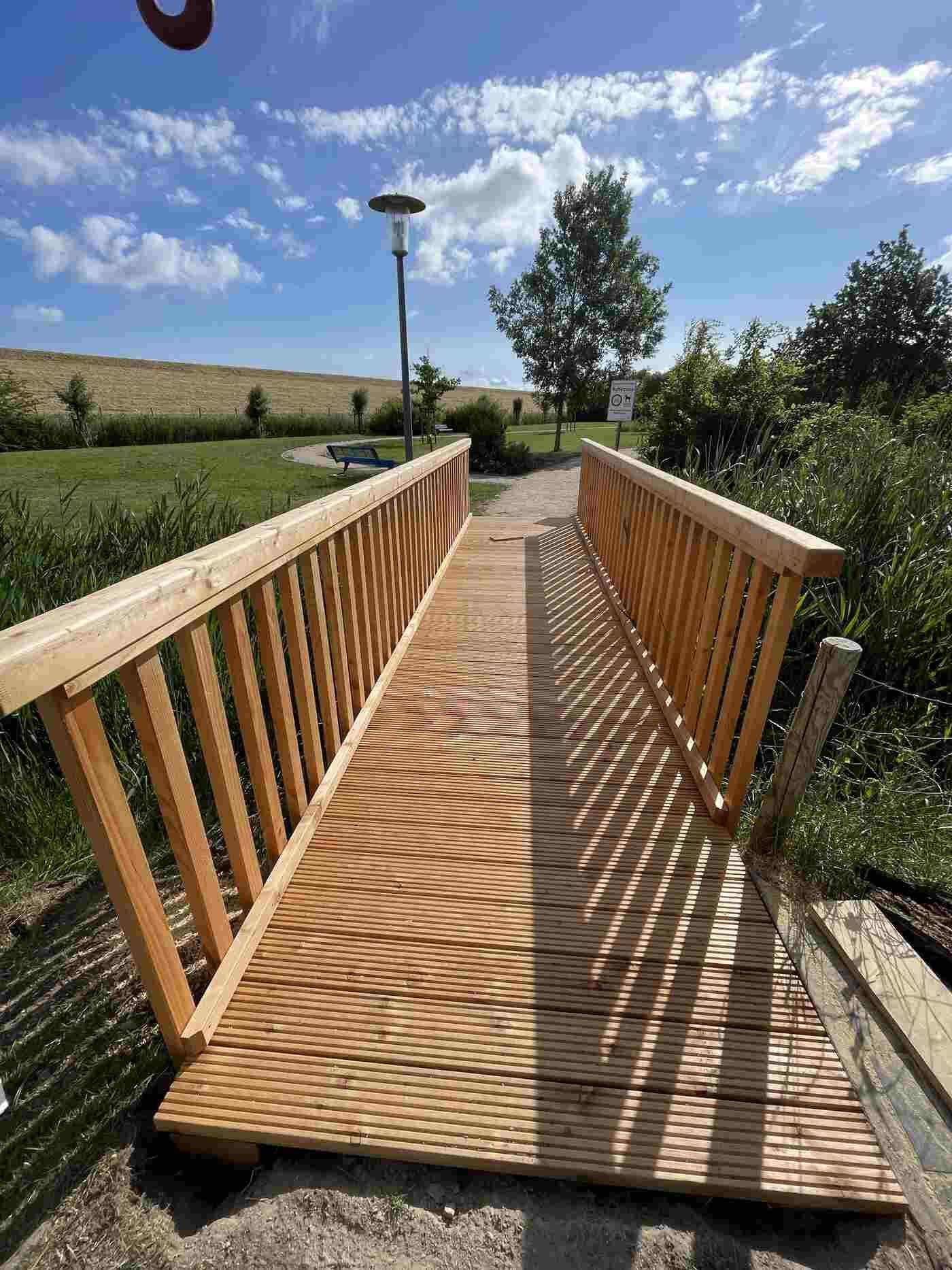 In einem Park wird eine Holzbrücke über einen Fluss gebaut.