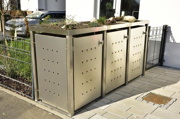 Sonderkonstruktionen Metallene Recyclingbox am Straßenrand neben Gehweg und Zaun, mit perforierten Paneelen und Mülltonnen im Inneren