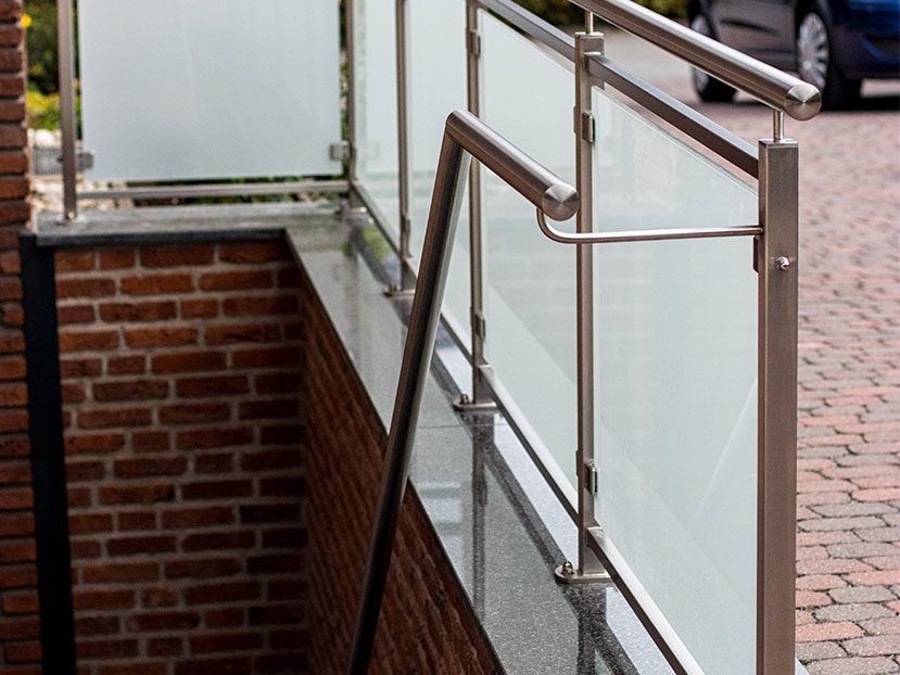 Edelstahlgeländer neben Milchglasscheiben über einem gemauerten Treppenhaus im Freien