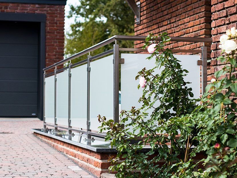 Moderne Rampe mit Glasgeländer neben einem Backsteinhaus und einer Garage in einer landschaftlich gestalteten Auffahrt