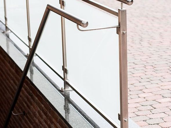 Geländer & Absturzsicherungen Edelstahlgeländer neben einem Schaufenster aus Glas, draußen nasser Gehweg und Ziegelsteinweg.