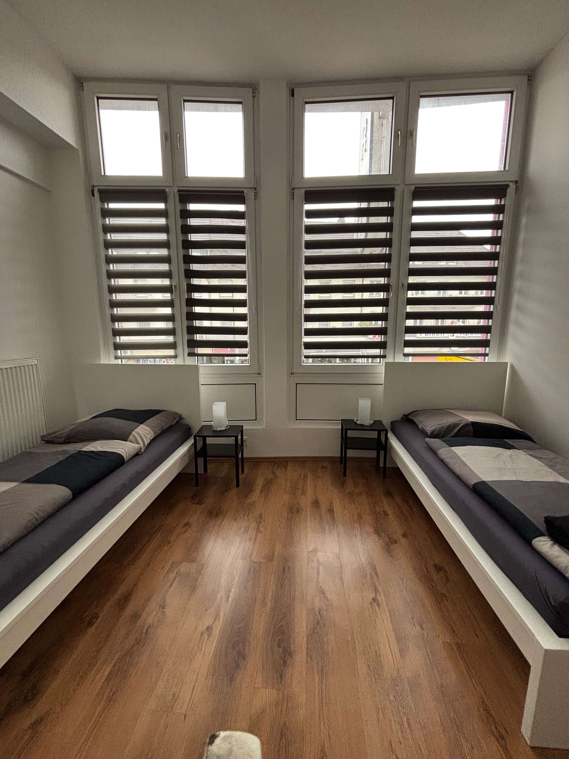 Ein Schlafzimmer mit zwei Betten und zwei Fenstern mit Jalousien.