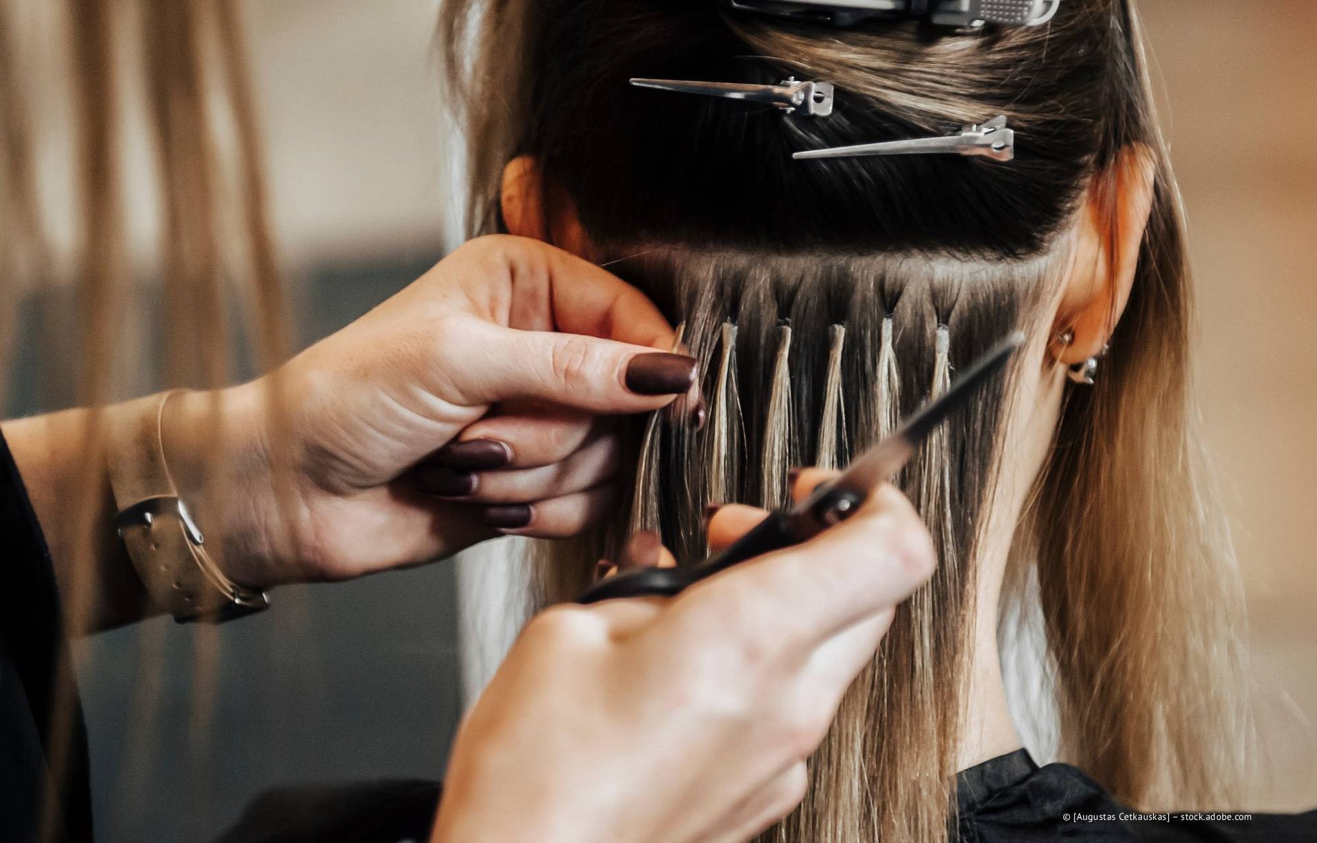 Hände, die Haarverlängerungen am natürlichen Haar einer Person anbringen; eine Salonumgebung.