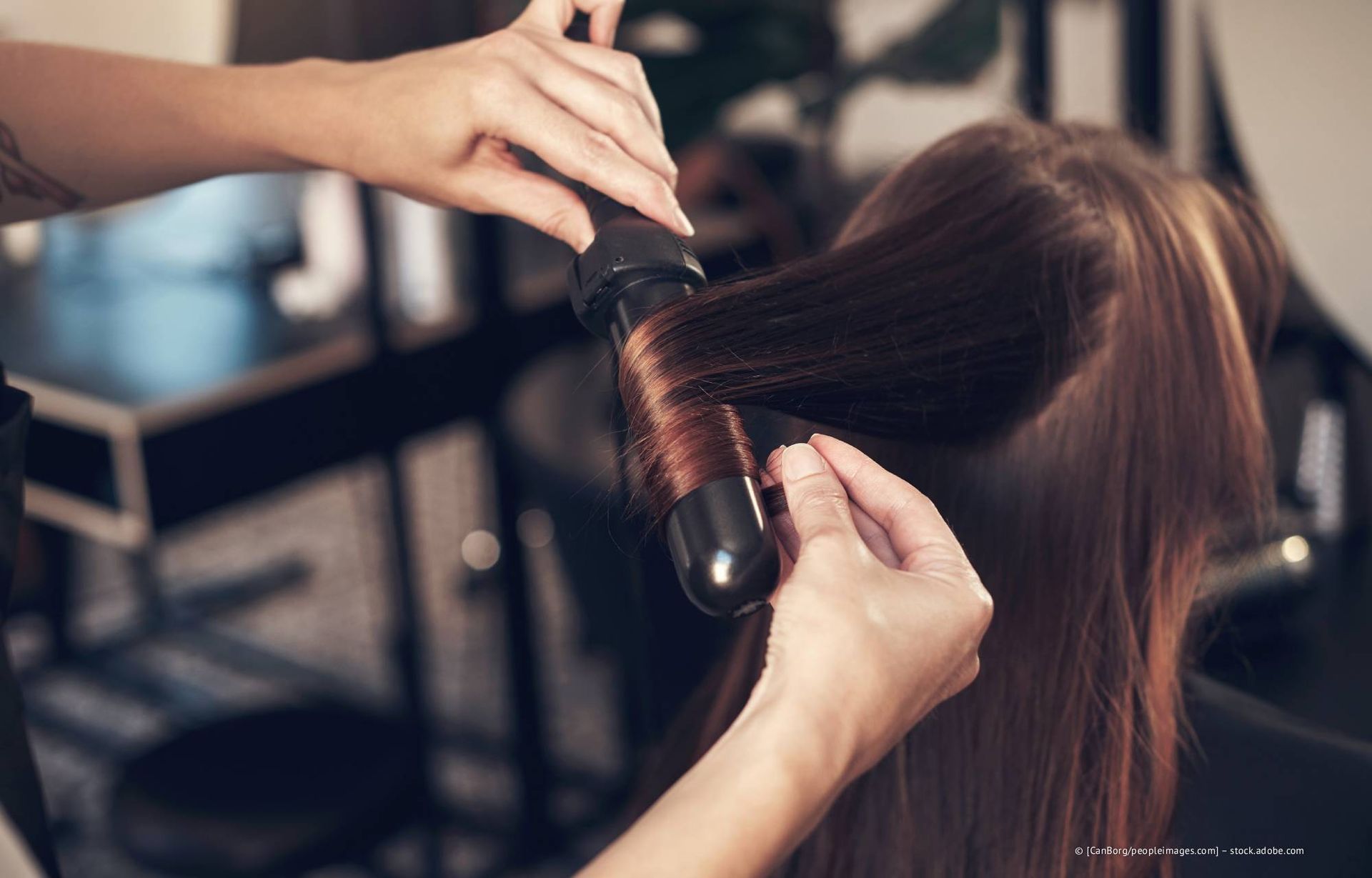 In einem Salon wird das Haar einer Person mit einem Lockenstab gestylt.