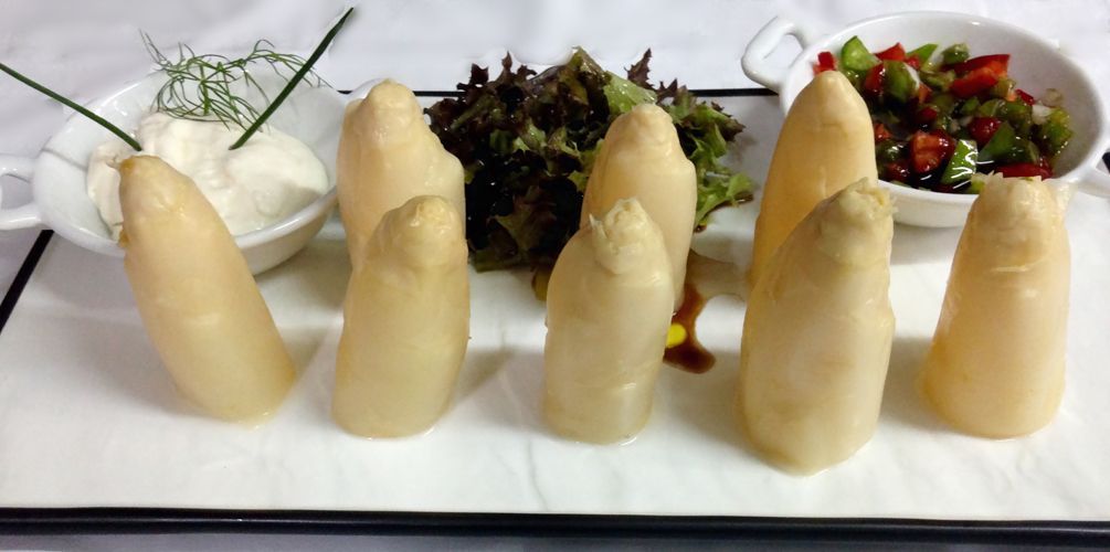 Un plato blanco cubierto de espárragos y un tazón de ensalada.