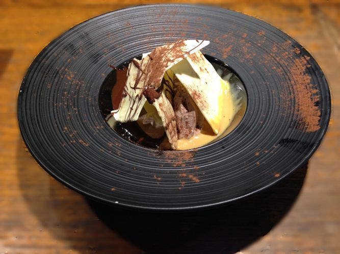 Un plato negro con un postre sobre una mesa de madera.