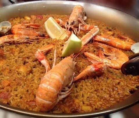 Una sartén llena de arroz, camarones, almejas y rodajas de limón.