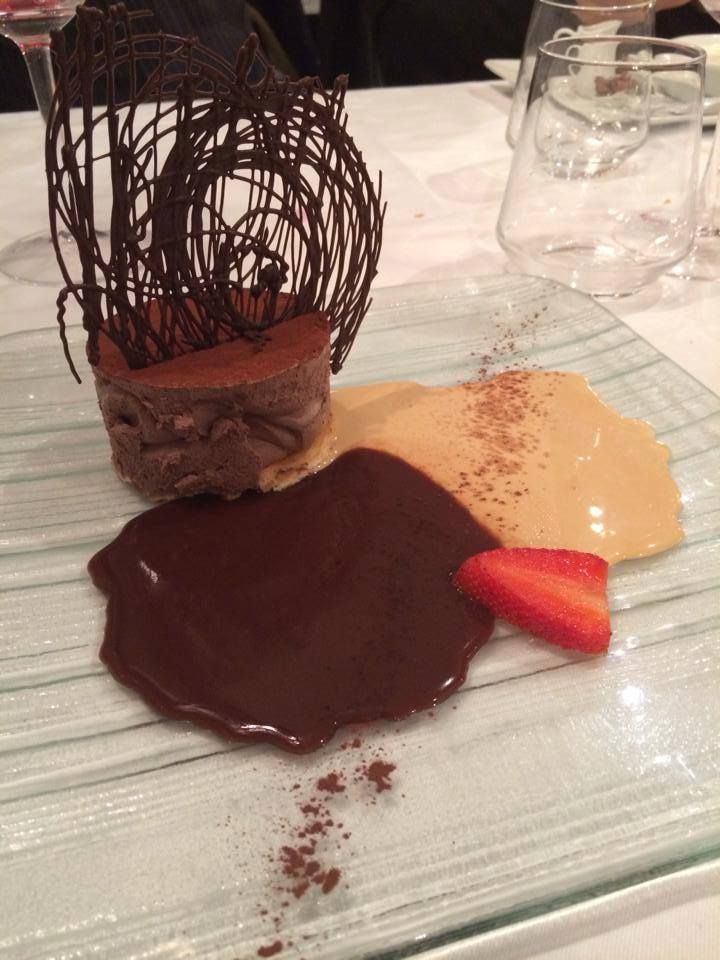 Un postre con salsa de chocolate y una fresa en un plato de cristal.