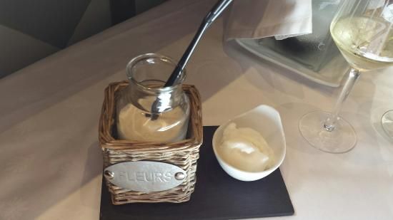 Un frasco de salsa con una cuchara dentro se encuentra sobre una mesa junto a un tazón de salsa y una copa de vino.