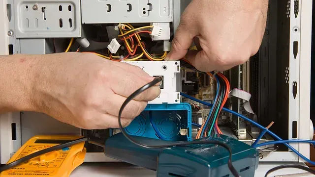 Una persona está trabajando en una computadora con un multímetro amarillo.