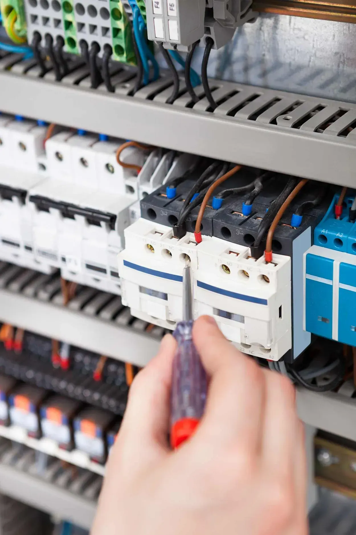 Una persona está trabajando en un panel eléctrico con un destornillador.